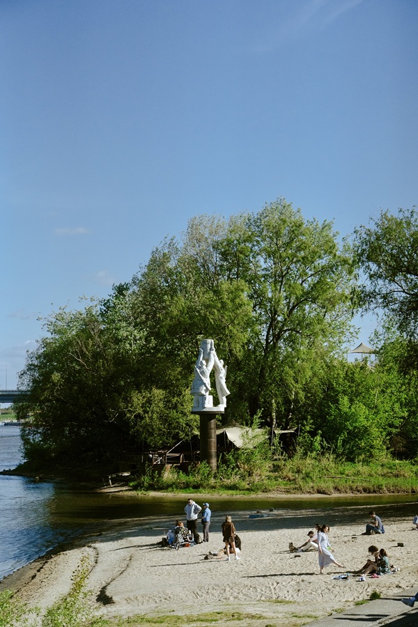 Plaża nad Wisłą w Warszawie z białą rzeźbą i wypoczywającymi mieszkańcami latem