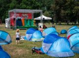 Dzieci oglądające interaktywny spektakl teatralny na scenie Warszawskiego Kocykowania w parku - namioty pop-up na trawie przed sceną
