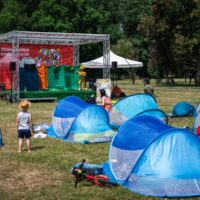 Dzieci oglądające interaktywny spektakl teatralny na scenie Warszawskiego Kocykowania w parku - namioty pop-up na trawie przed sceną