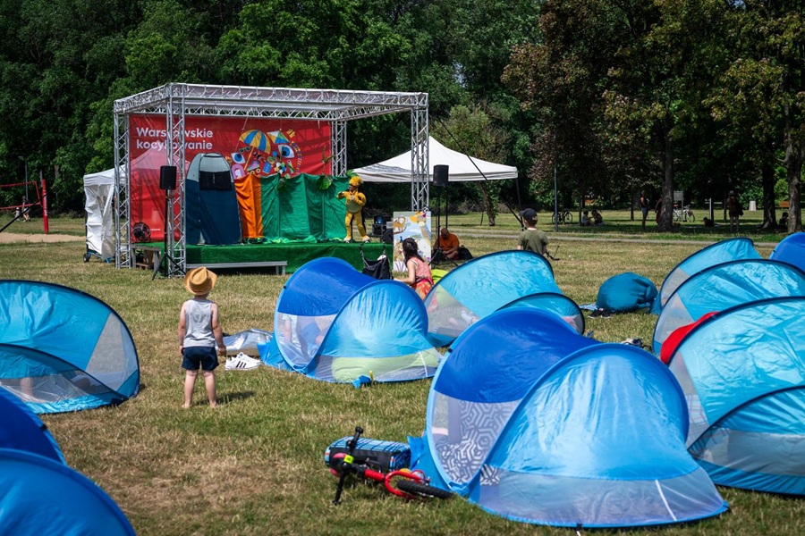 Dzieci oglądające interaktywny spektakl teatralny na scenie Warszawskiego Kocykowania w parku - namioty pop-up na trawie przed sceną